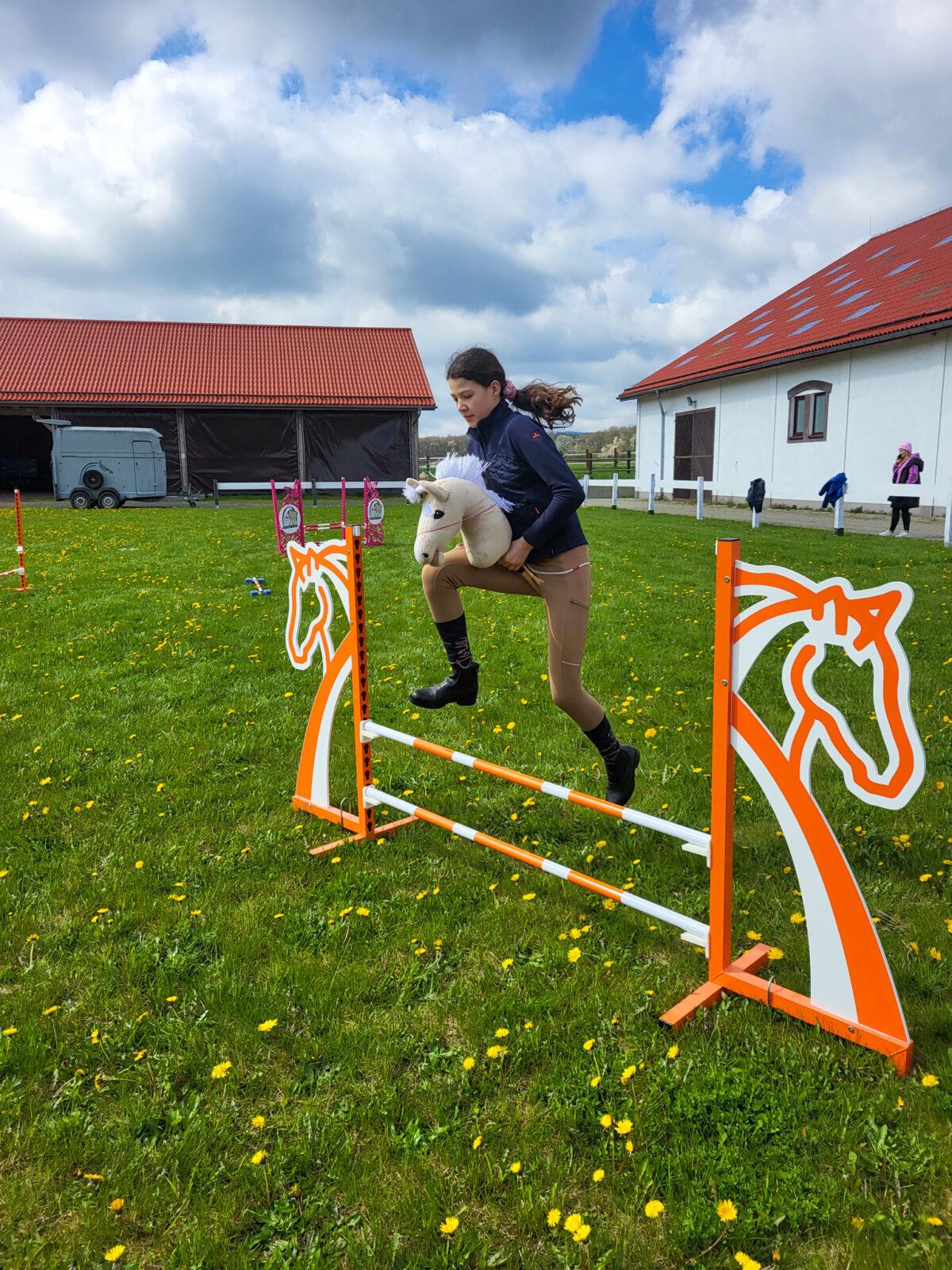 dziewczynka skacze przez przeszkodę na hobby horse