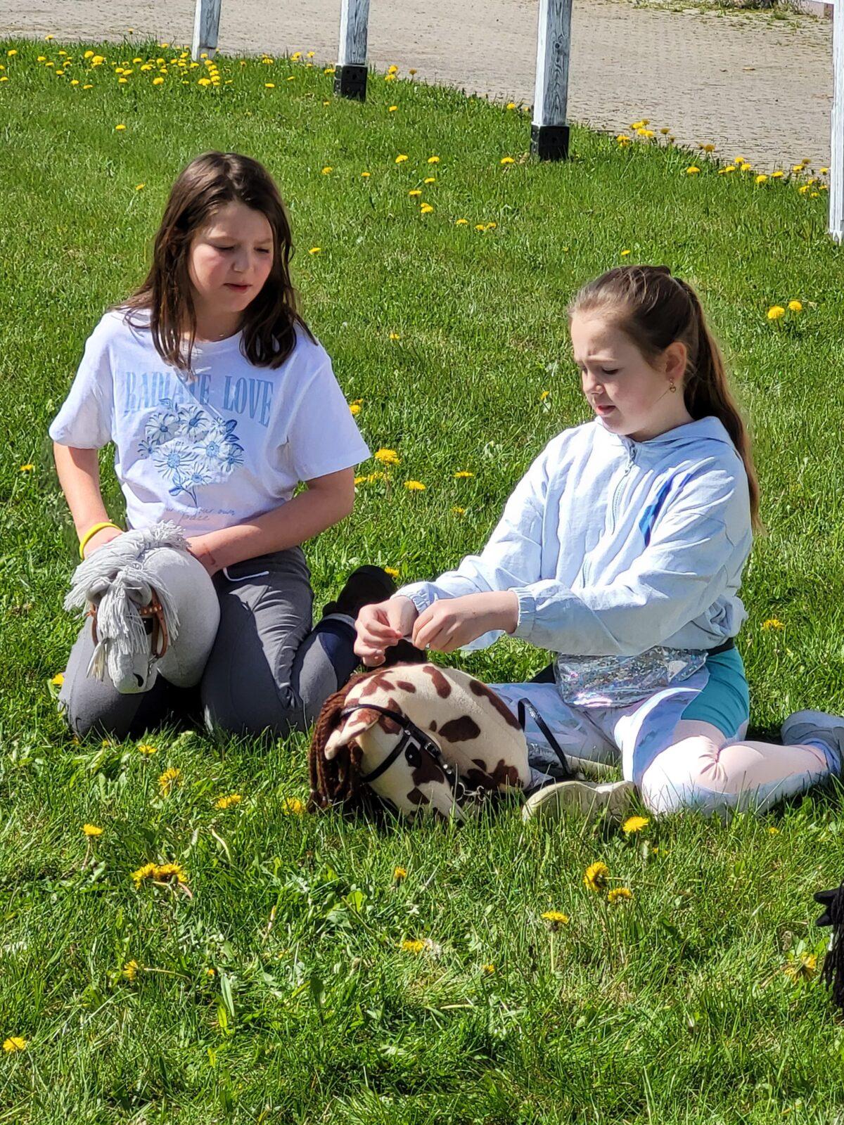 dziewczynki siedzą na trawie i bawią się swoimi hobby horse